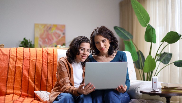 A mother and a child sitting on a sofa looking at a laptop