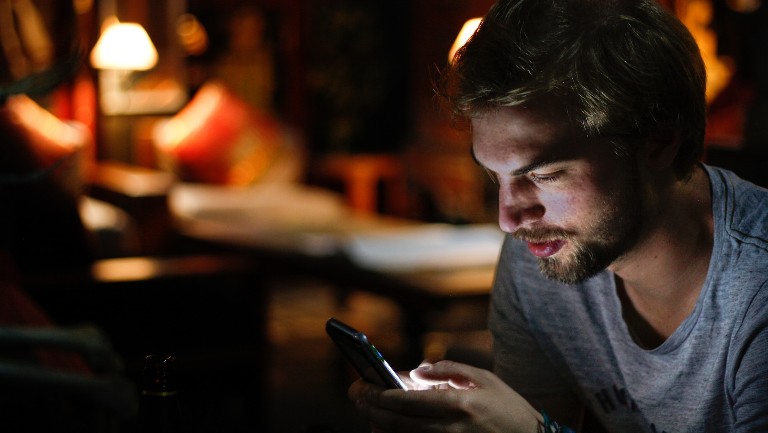 Young man looking at his mobile phone in the dark
