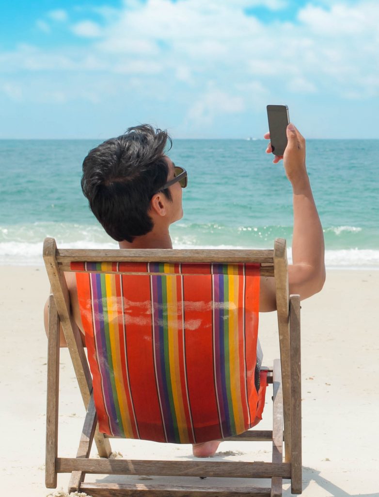 Man sitting on a deck chair on holiday using his mobile phone.